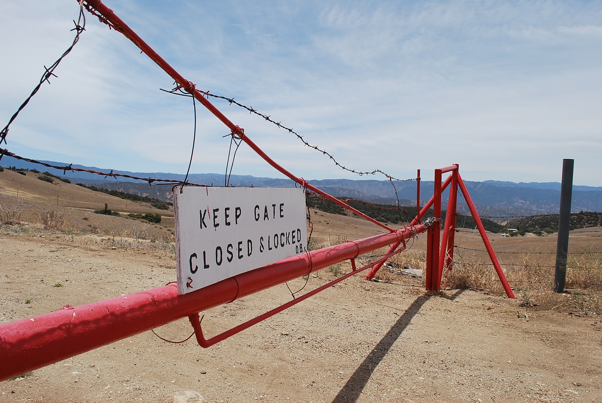 Unwelcome looking gate in arid landscape with barbed wire saying keep gate closed and locked